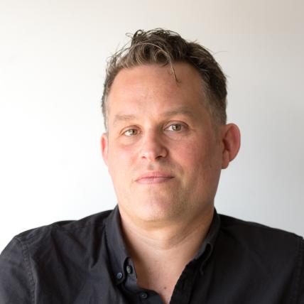 Headshot of Noah Simblist wearing a button-up black shirt in front of a plain white background