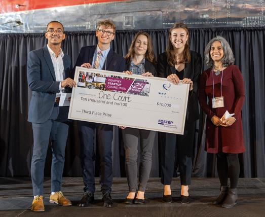 Four students holding prize check standing with adviser