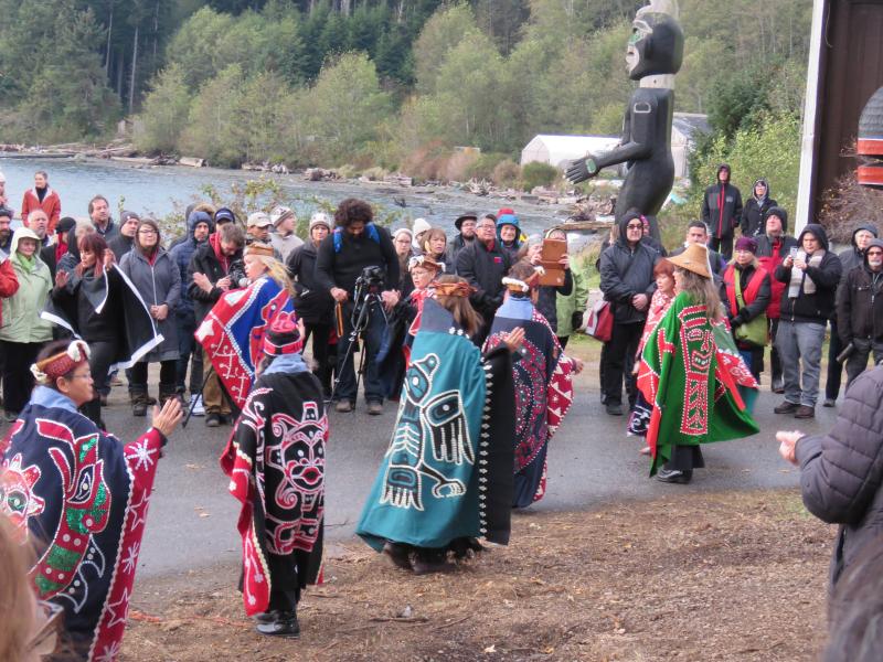 Women dancing in colorful regalia at totem pole raising
