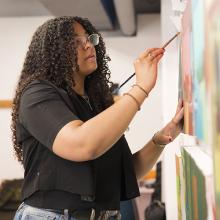 Kyra Wolfenbarger standing and painting in an art studio.
