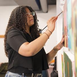 Kyra Wolfenbarger standing and painting in an art studio.