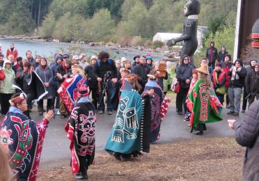 Women dancing in colorful regalia at totem pole raising
