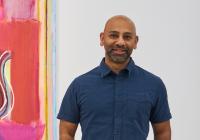 Sangram Majumdar standing in front of one of his paintings.