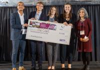Four students holding prize check standing with adviser