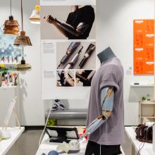 Exhibition view with hanging poster and display mannequin on table.