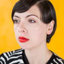 Portrait of Natalie Krick wearing a zibra-stripped shirt and in front of a golden yellow background