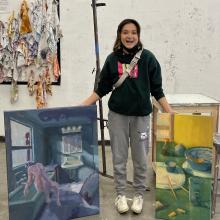 Zoë Tsai standing in her studio with a painting by each leg