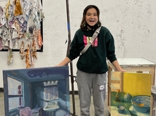 Zoë Tsai standing in her studio with a painting by each leg